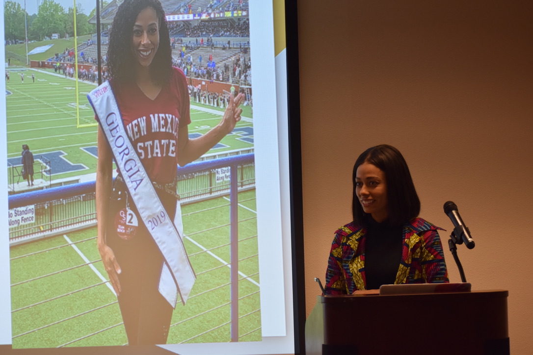 Sara Joyner speaking in front a projected photo of herself as Miss Georgiaduring the 2020 Black History Month Event. 