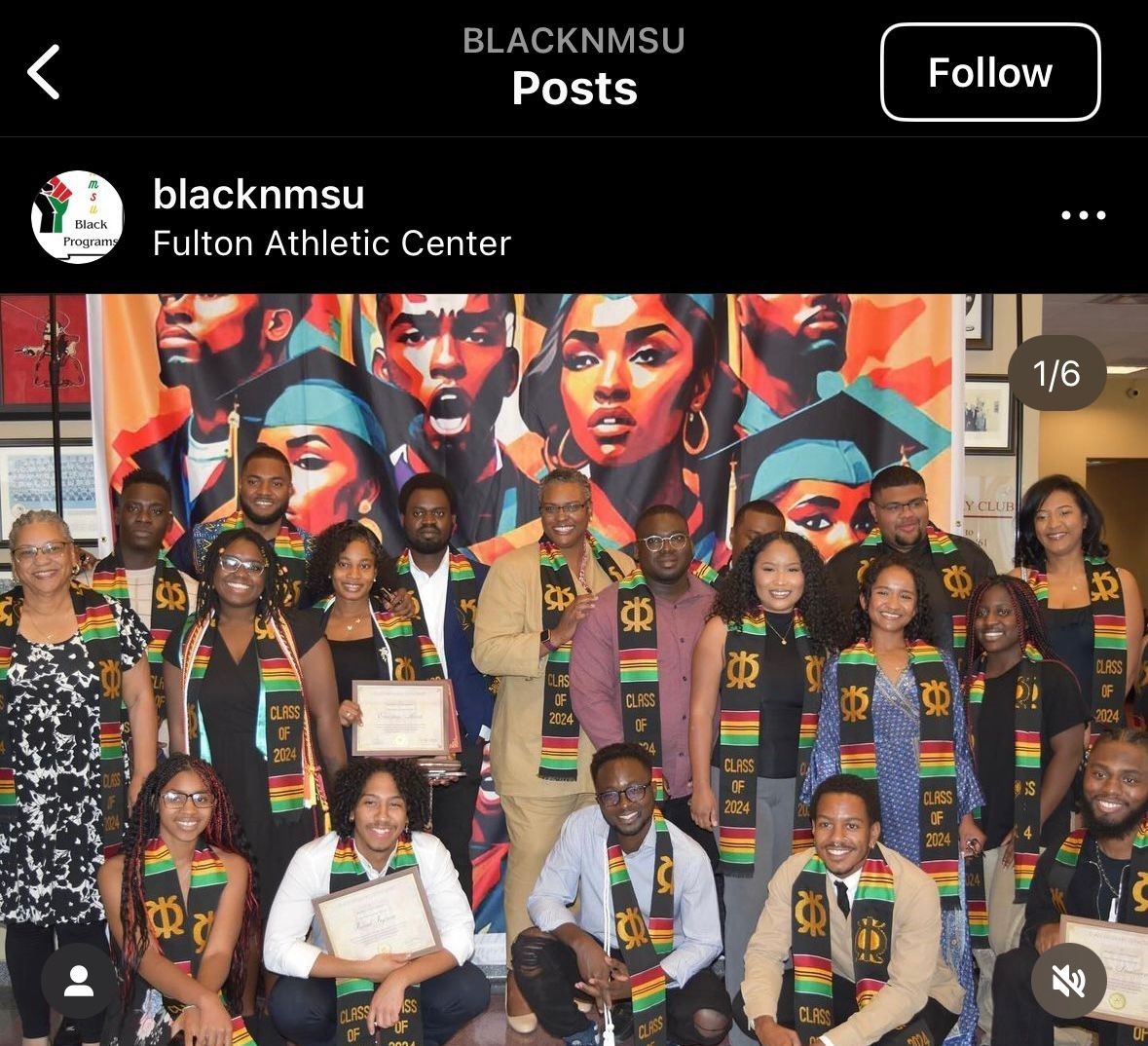The image shows a group of people posing for a picture, likely in celebration or recognition event. They are all wearing black, green, and red stoles that say "Class of 2024". Everyone in the group is smiling. In the background, there is a vibrant mural depicting several faces in colorful, abstract styles, including a portrait of a woman and a man wearing a graduation cap. The group consists of around twenty individuals, both sitting and standing, in an indoor setting. Some people are holding certificates. Above the group, there is a black banner featuring the words "BLACKNMSU" at the top and an Instagram-style interface showing the account "blacknmsu," which is located at the Fulton Athletic Center.